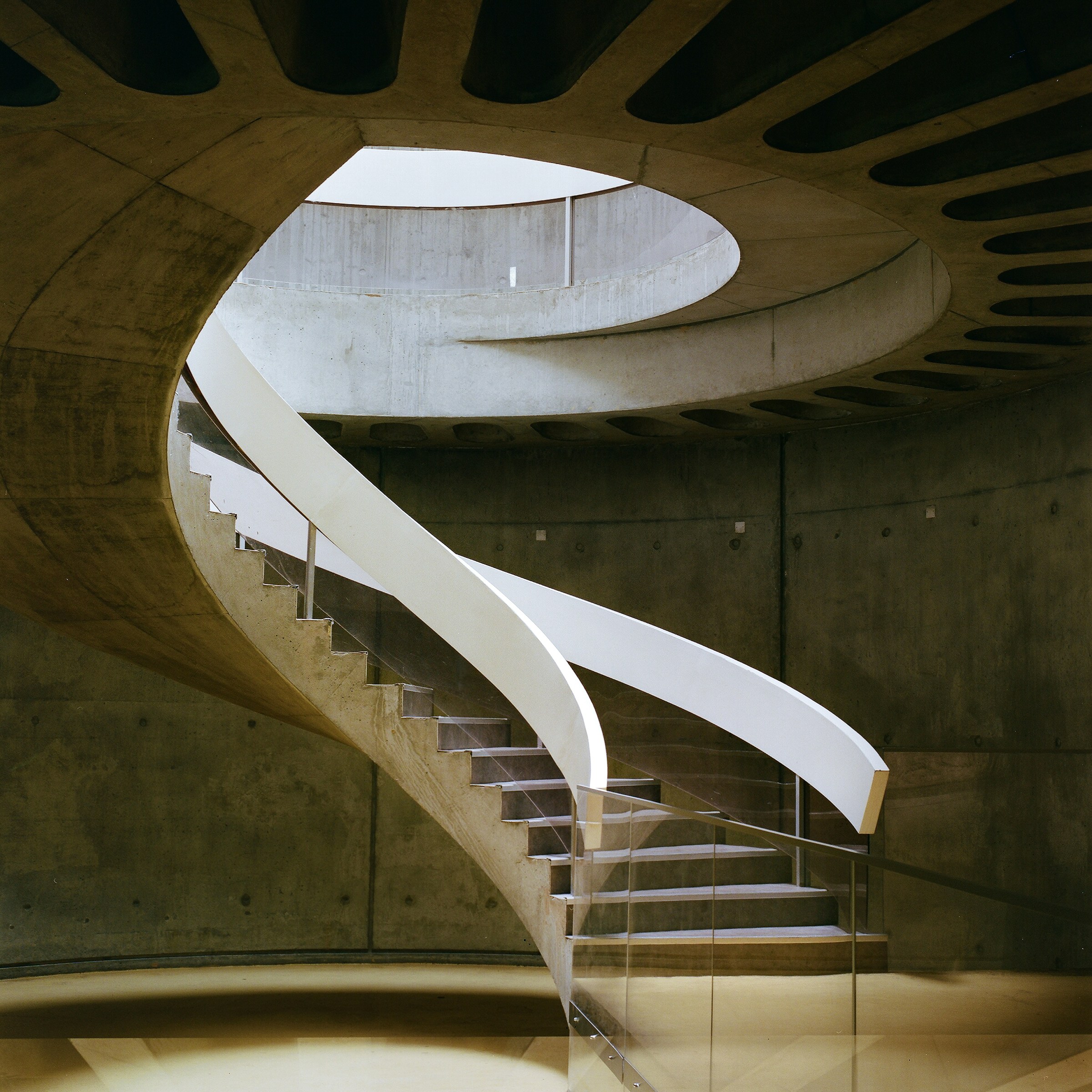 A sculptural concrete spiral staircase ascending inside a modern building
